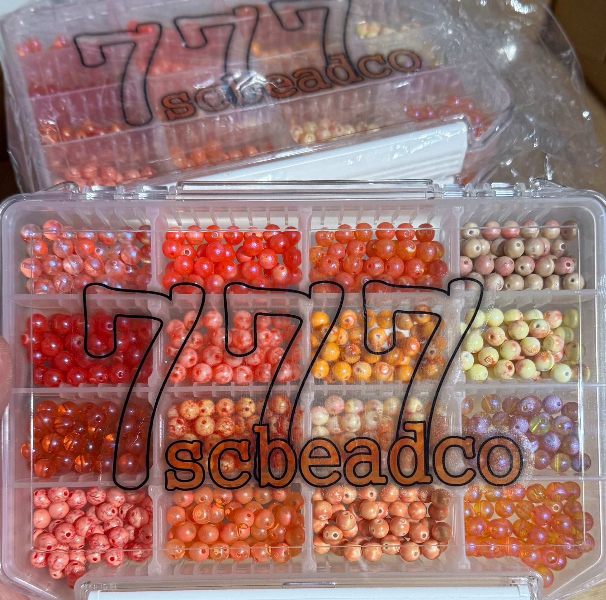 Clear plastic container with compartments filled with small beads, branded '777 scbeadco'.