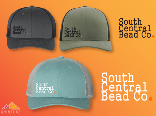 A collection of three trucker hats in gray, green, and blue, each featuring an embroidered logo of the South Central Bead Co. on the front.
